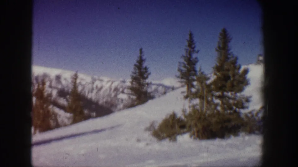 8mm panning shot of a sunlit ski slope circa 1961, likely Aspen, Colorado, showing conifers and snow-covered terrain with a mountain ridge in the background.