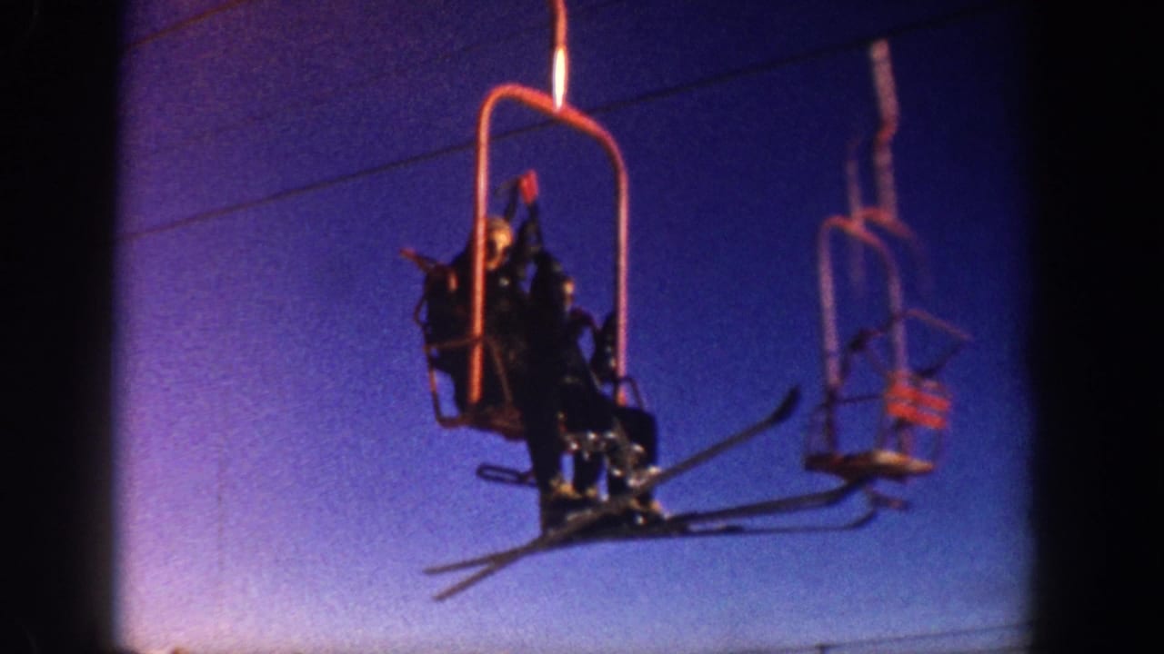 Skiers riding a red open chairlift, shot from below against a blue-purple sky — consistent with Aspen, Colorado, circa 1961, captured on 8mm home-movie film.