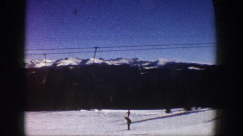 Continuation wide shot of snow-covered slopes and distant mountain peaks with lift cables and a lone skier; consistent with a 1961 8mm home-movie sequence at Aspen, Colorado.