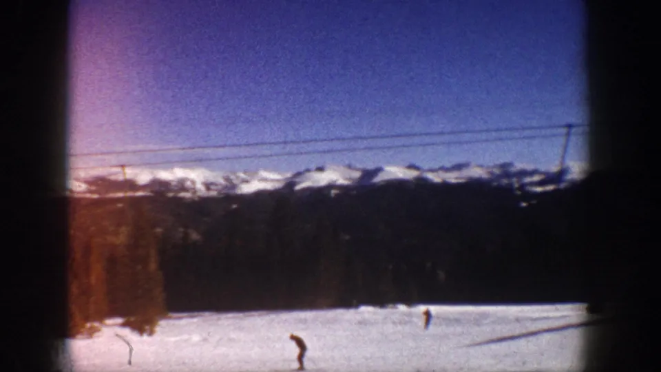 Single skier on a snow slope with ski lift cables and a conifer-edged mountain range, consistent with Aspen, Colorado circa 1961 per clip metadata.