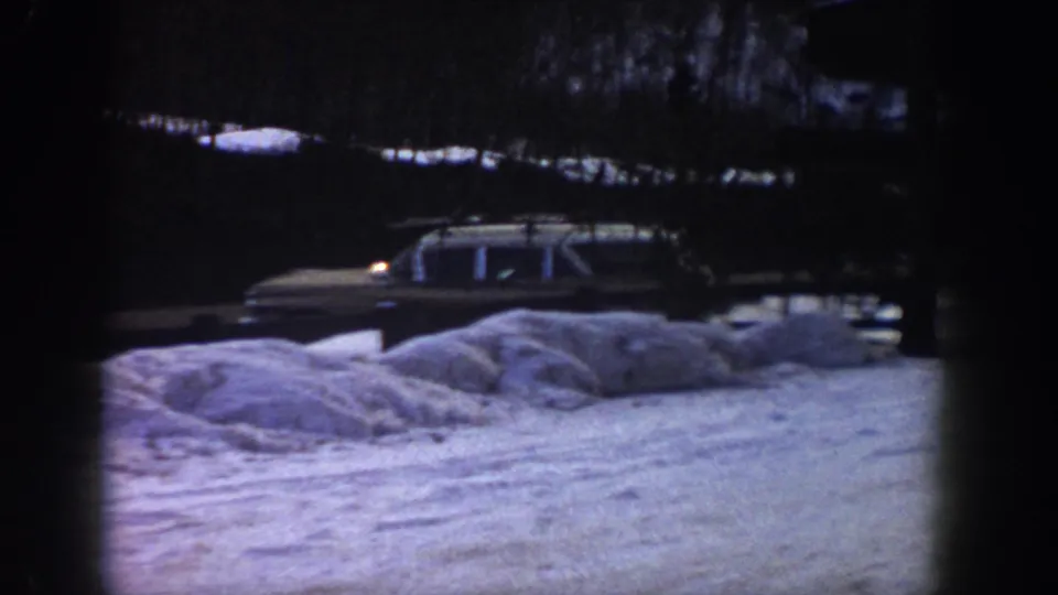 Early-1960s American station wagon with roof rack on a snowy mountain road, likely Aspen area, 1961, shot on 8mm home-movie film.