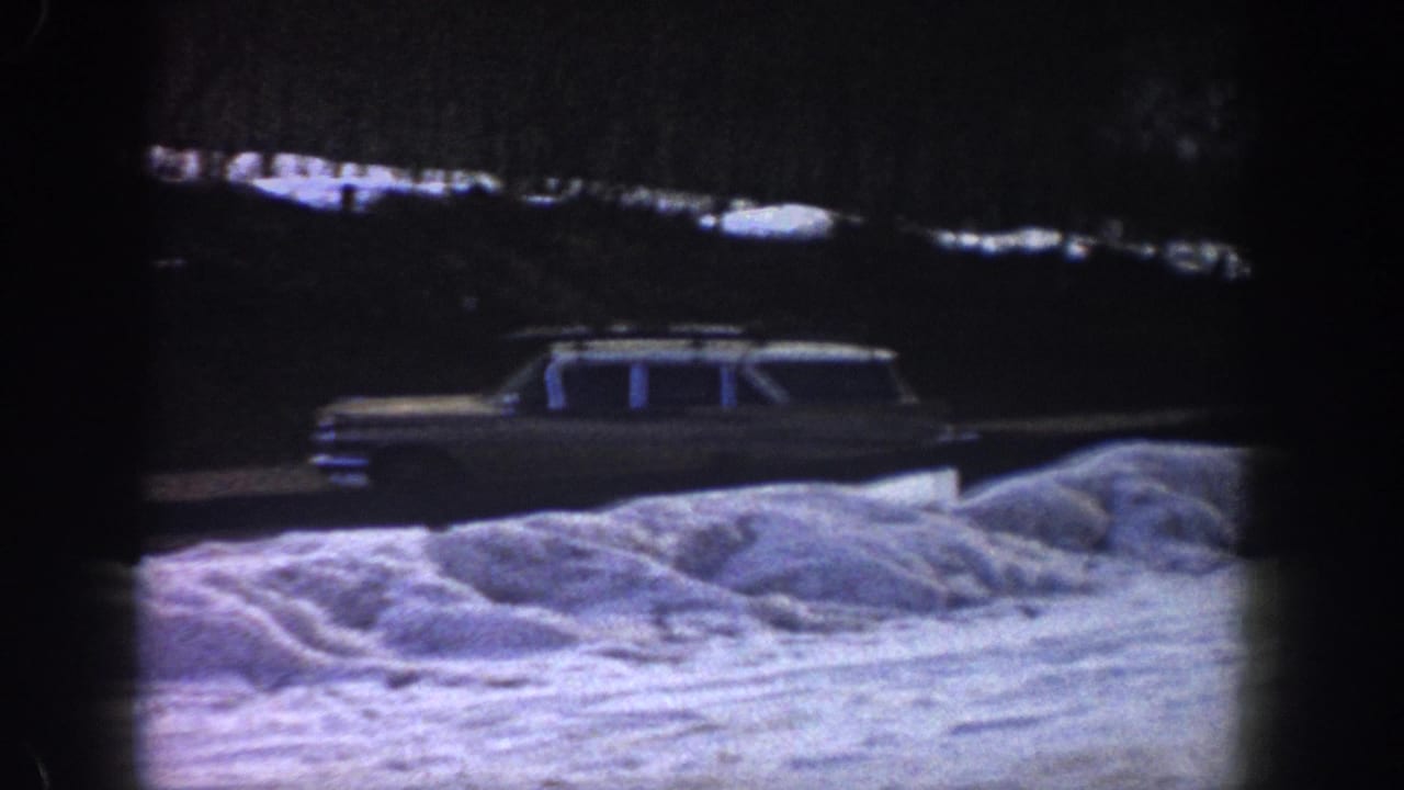 Early-1960s American station wagon on a snow-covered mountain road, possibly Aspen, Colorado, 1961, with characteristic 8mm blue-purple color shift.