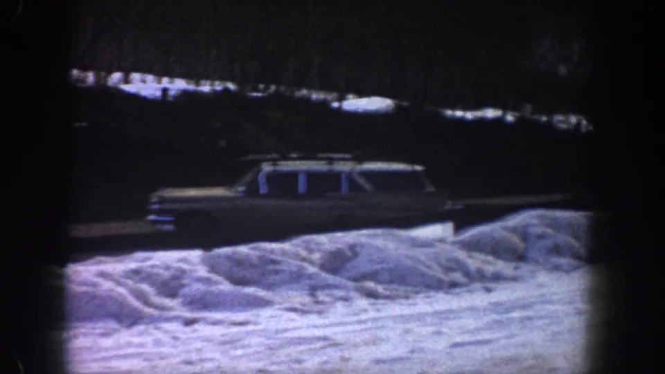 Early-1960s American station wagon on a snow-covered mountain road, possibly Aspen, Colorado, 1961, with characteristic 8mm blue-purple color shift.