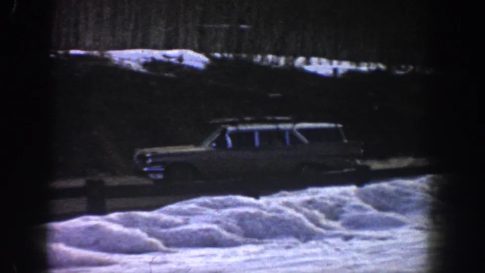 Boxy early-1960s American station wagon with roof luggage rack on a snowy mountain road, attributed to Aspen, Colorado, 1961, on 8mm film.