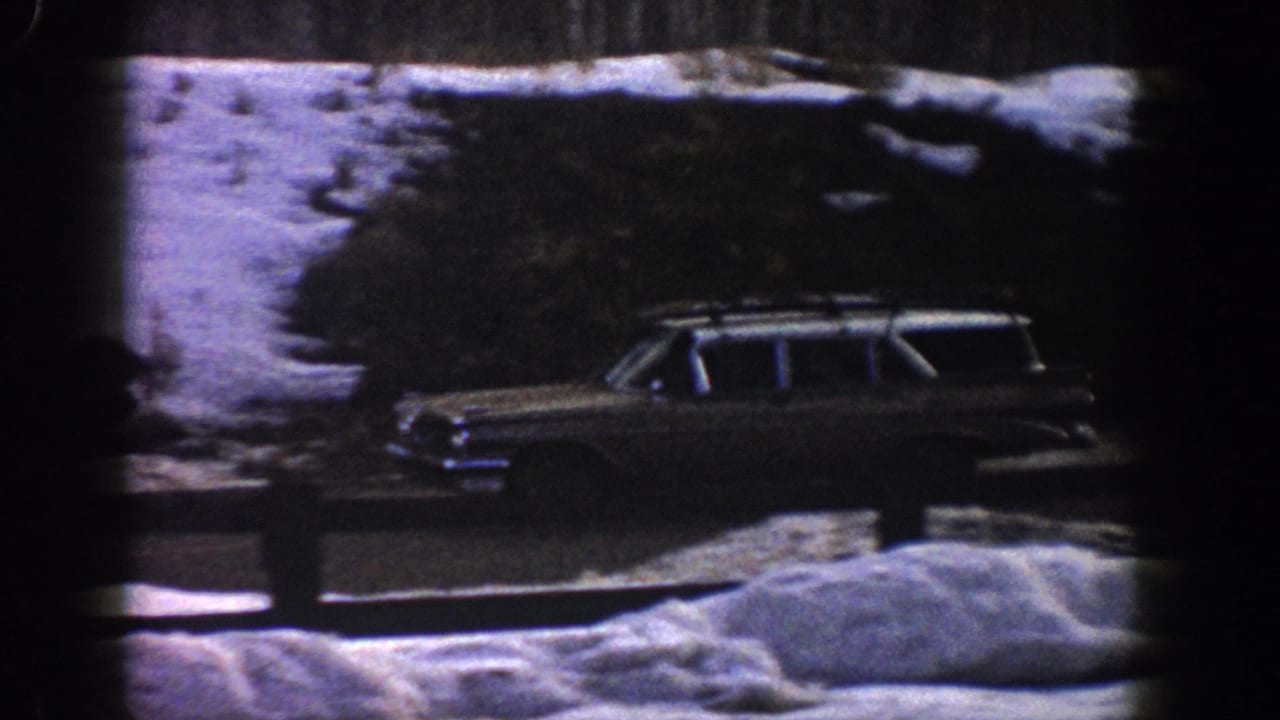 Early-1960s station wagon with roof rack rolling along a snow-lined road in a Colorado mountain setting, circa 1961 8mm home movie.