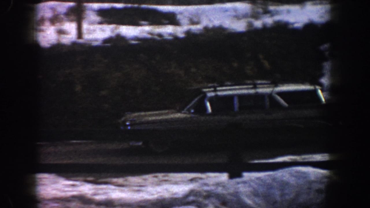 Station wagon with roof rack advancing along a snow-banked mountain road; utility pole visible in the background.
