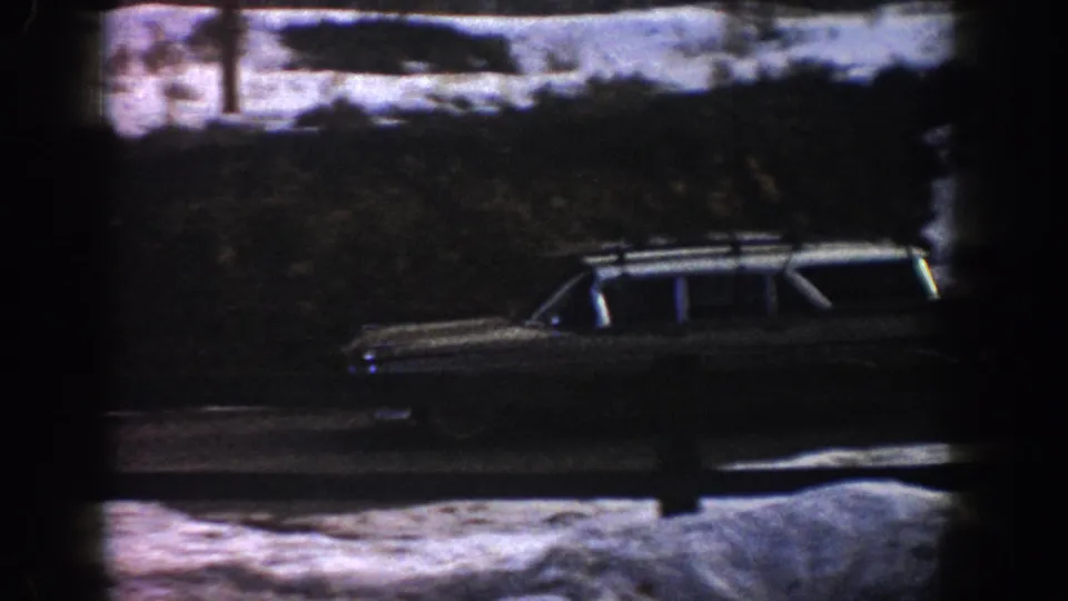 Same early-1960s station wagon advancing along a snow-lined mountain road with a utility pole in the background; Colorado mountain area, circa 1961 8mm home movie.