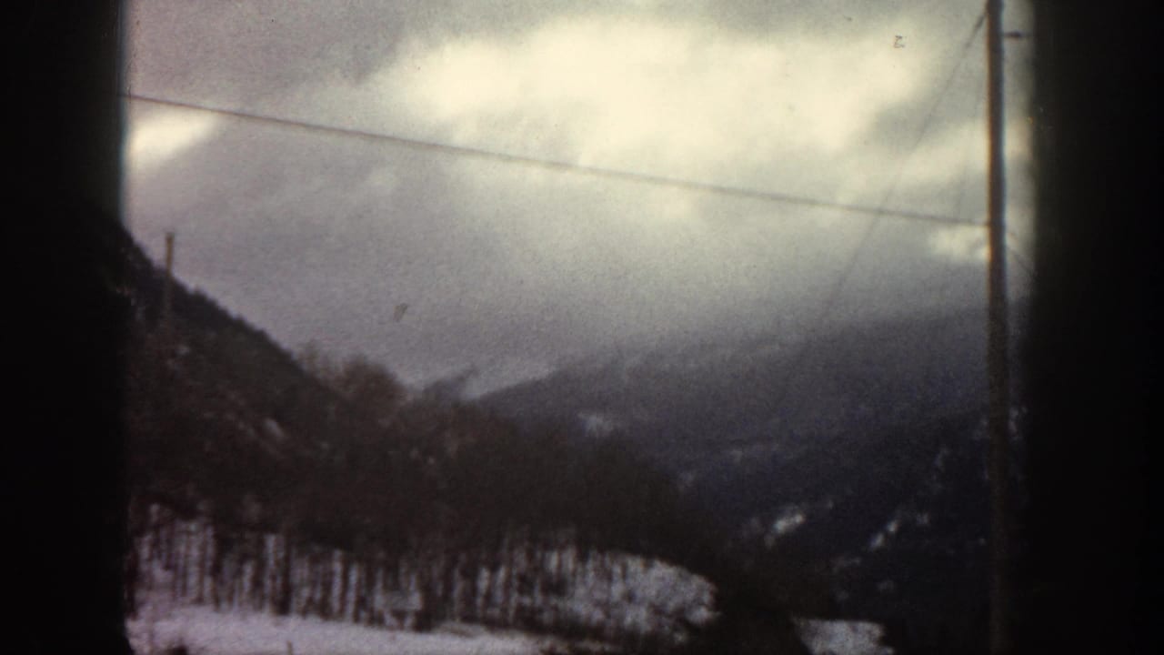 8mm home movie frame of snow-dusted mountain slopes, bare trees, and power lines under heavy cloud cover, likely Aspen, Colorado, c. 1961.