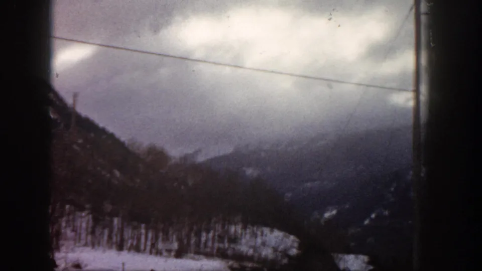 Continuous 8mm driving shot of snow-covered Colorado mountain slopes and power lines under overcast winter sky, c. 1961.