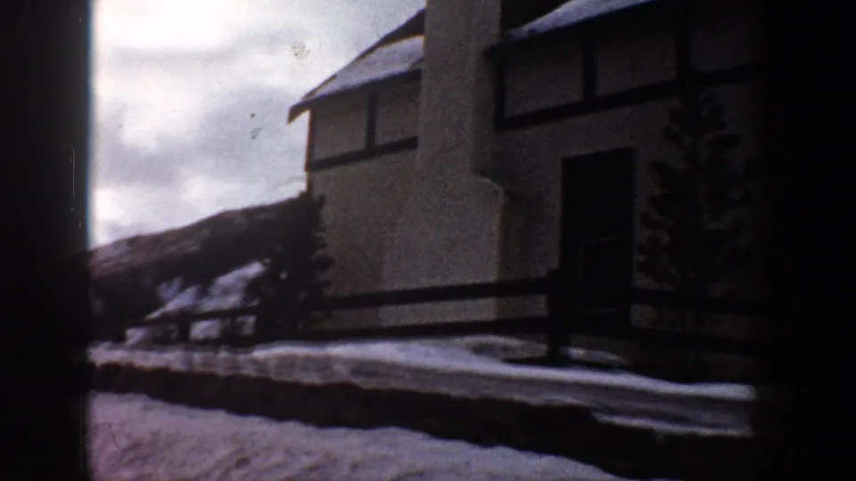 8mm home movie frame of a mid-century multi-story building with snowy roof and small evergreen tree, Aspen, Colorado area, c. 1961.