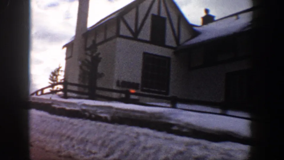 8mm frame of a mid-century Alpine-style gabled building with dark timber trim and snow-covered surroundings, Aspen, Colorado area, c. 1961.