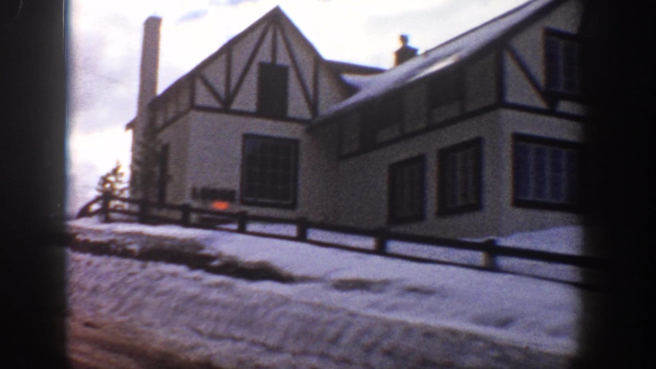 Large Tudor Revival residence in Aspen, Colorado, circa 1961, seen from a moving vehicle; snow on roof and grounds, split-rail fence, overcast sky.