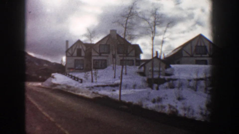 Tudor Revival house seen from a departing vehicle angle along a snowy mountain road, Aspen Colorado, 1961; bare trees and hillside in background.