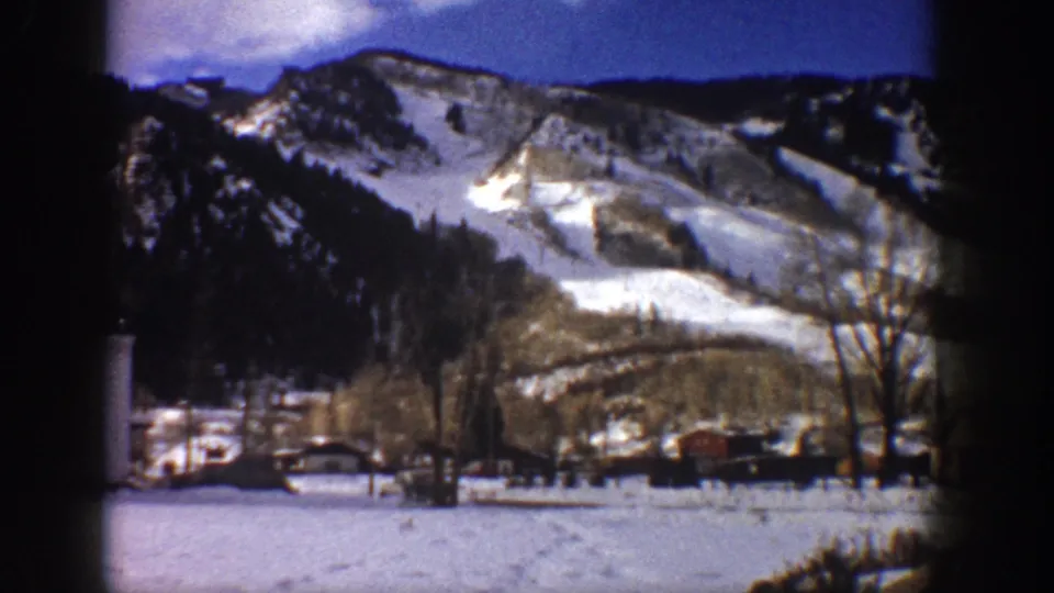 8mm home movie frame of a large snow-dusted mountain and snow-covered valley with scattered small structures, possibly Aspen, Colorado, circa 1961.