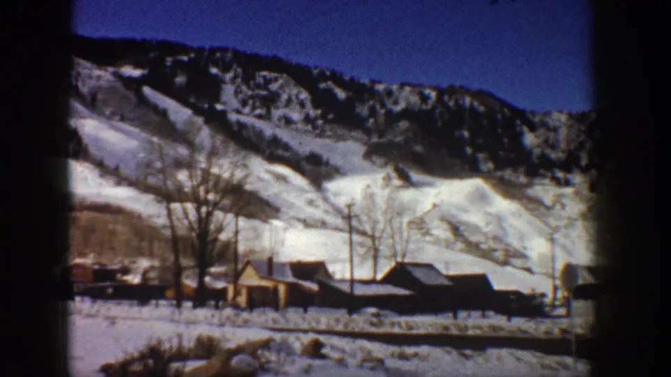 8mm end frame, Aspen, Colorado, c.1961 — pan endpoint across valley showing wooden buildings, utility poles, and bare trees backed by steep snow-covered slopes.