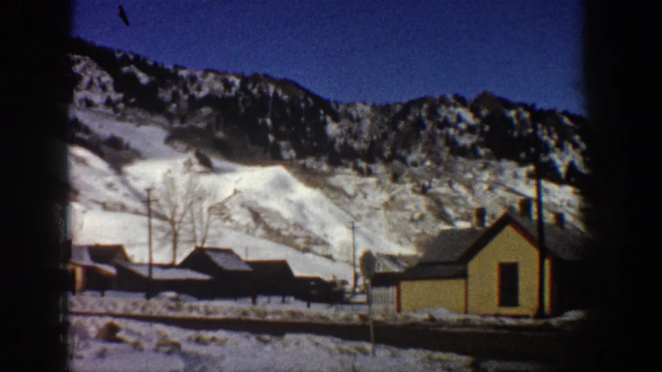 Prominent gabled building and utility poles in a winter valley with a snow-covered mountain backdrop, Aspen, Colorado area, circa 1961, 8mm color.