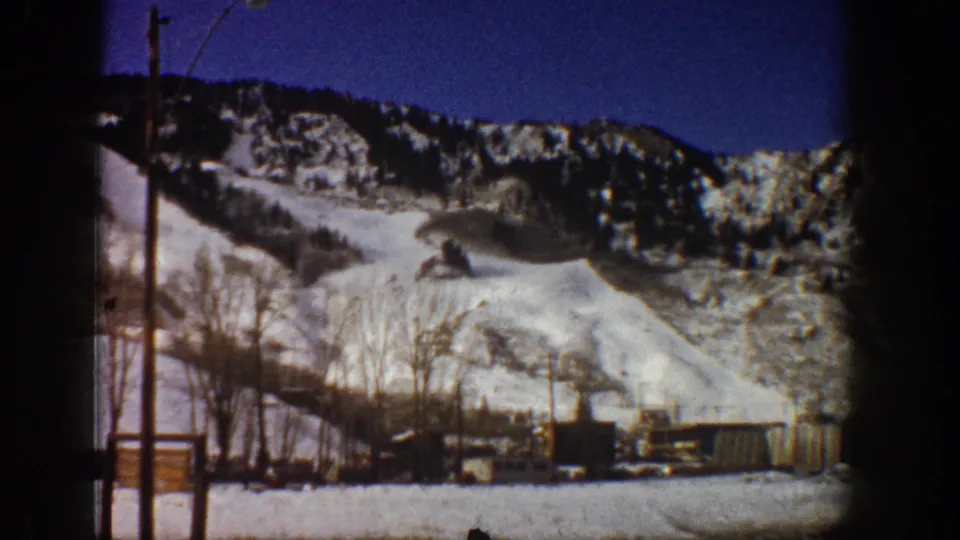 End of 8mm pan, Aspen, Colorado, c.1961 — snow-covered mountain slopes, bare aspen trees, small structures, and utility poles against deep blue winter sky.