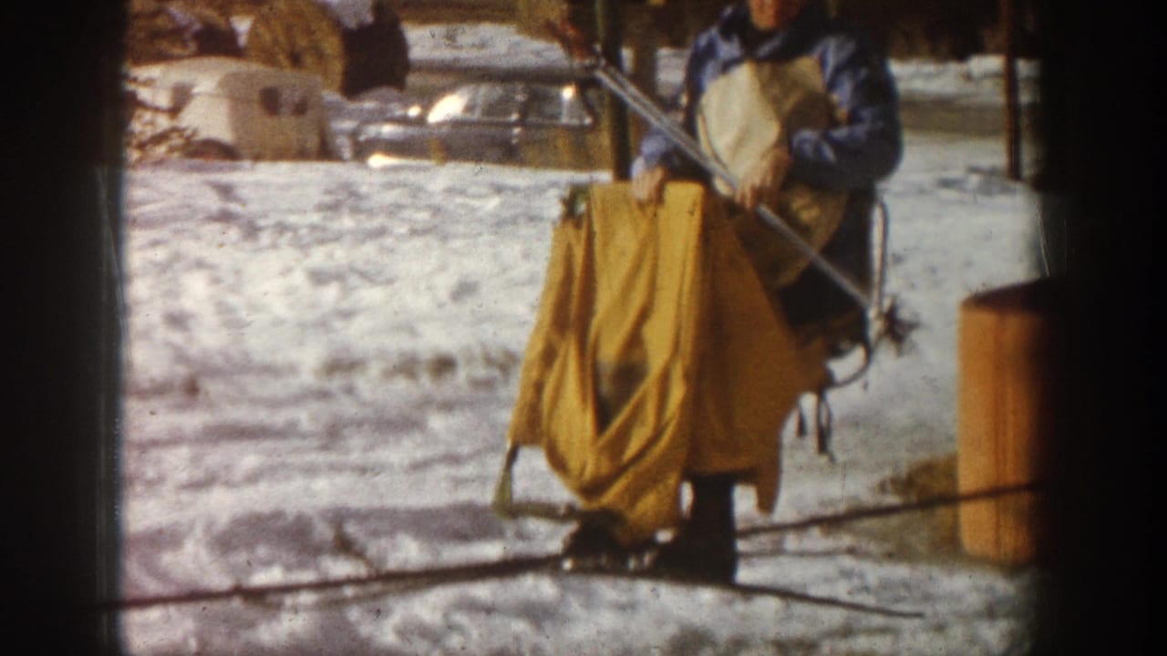 Man in blue ski jacket at ski lift loading station with yellow chair apron, Aspen Colorado area circa 1961, 8mm home movie.