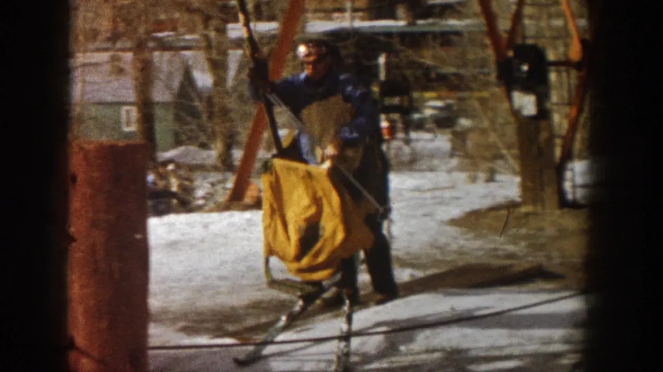 Man in blue ski jacket at chair lift base with a second person near the lift operator area, Aspen area circa 1961, 8mm home movie.