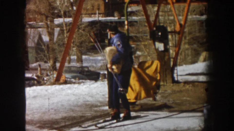 Man in blue ski jacket with skis at the chair lift base, yellow chair apron and bare deciduous trees visible, Aspen Colorado area circa 1961.