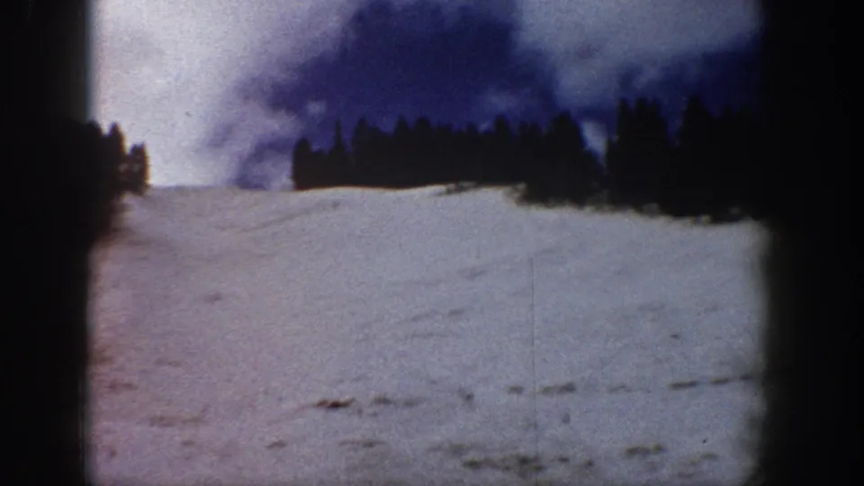 Wide view of a snow-covered slope and conifer forest at a mountain ski area, showing a characteristic warm color shift in the aging 8mm film stock; consistent with Colorado mountain terrain, circa 1961.