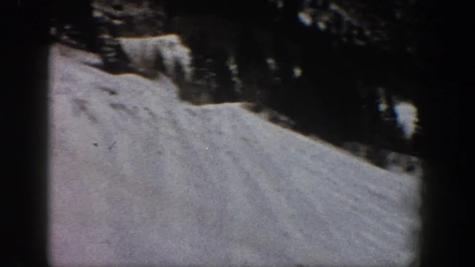 8mm home movie frame showing a broad snow slope and a stand of dark conifers at upper right, consistent with Aspen, Colorado, circa 1961.