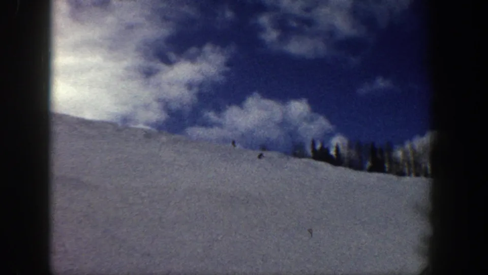 Wide 8mm shot of a snowy alpine slope under vivid blue sky with cumulus clouds and a distant treeline, likely Aspen, Colorado, circa 1961.