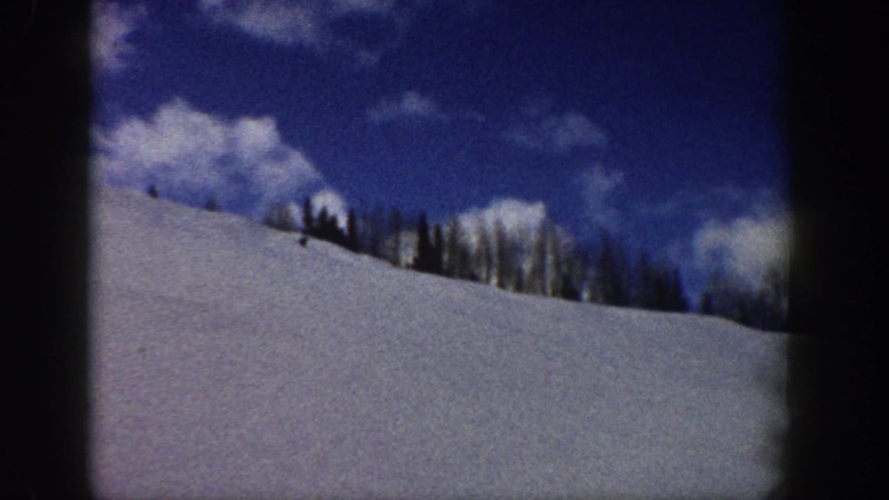8mm home movie frame of a wide snow-covered mountainside with a conifer treeline, cumulus clouds, and a small indistinct figure near the trees, Aspen Colorado area, circa 1961.