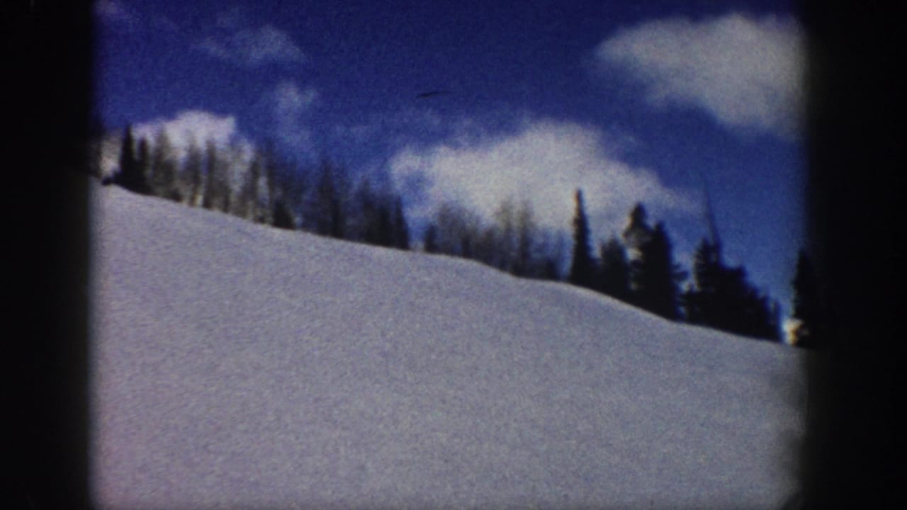 Alpine snow slope with mixed conifer and bare deciduous treeline under blue sky; 8mm film, circa 1961.