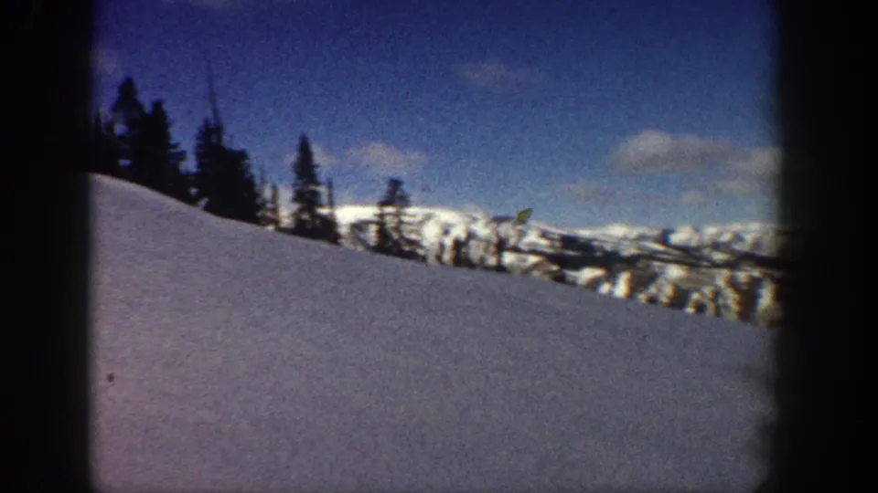 8mm home movie frame of a snow slope with a prominent conifer treeline and snow-covered distant peaks on the horizon, Aspen Colorado area, circa 1961.