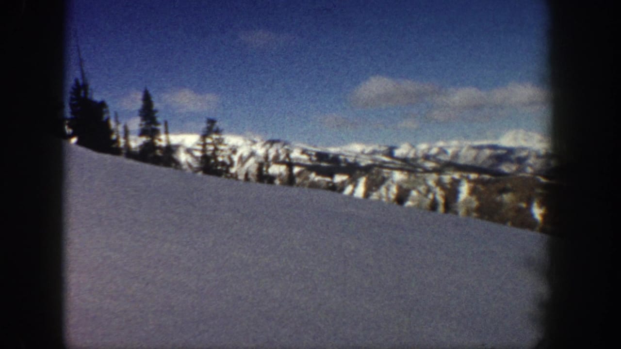Wide 8mm shot of snow-covered peaks and conifer forest in the Aspen, Colorado area, circa 1961, in bright winter sunlight.