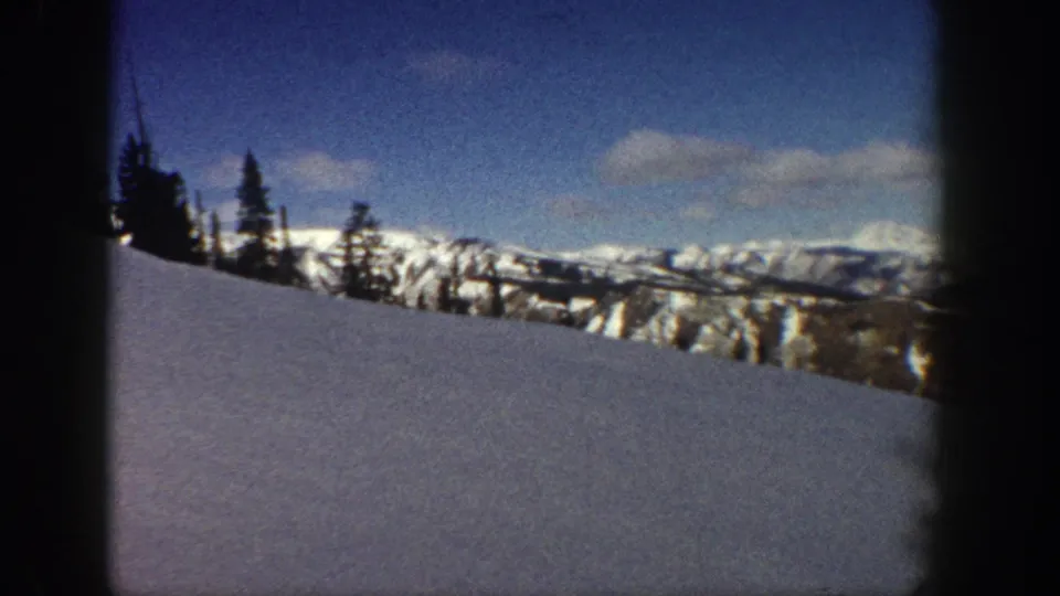Wide 8mm shot of snow-covered peaks and conifer forest in the Aspen, Colorado area, circa 1961, in bright winter sunlight.