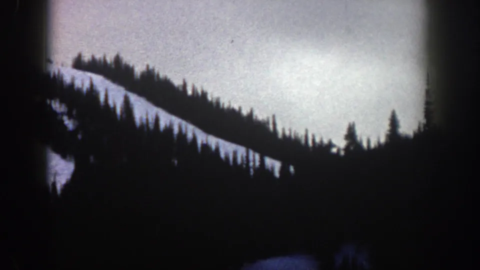 Underexposed 8mm frame showing a dark conifer ridgeline against pale sky in the Aspen, Colorado area, circa 1961.