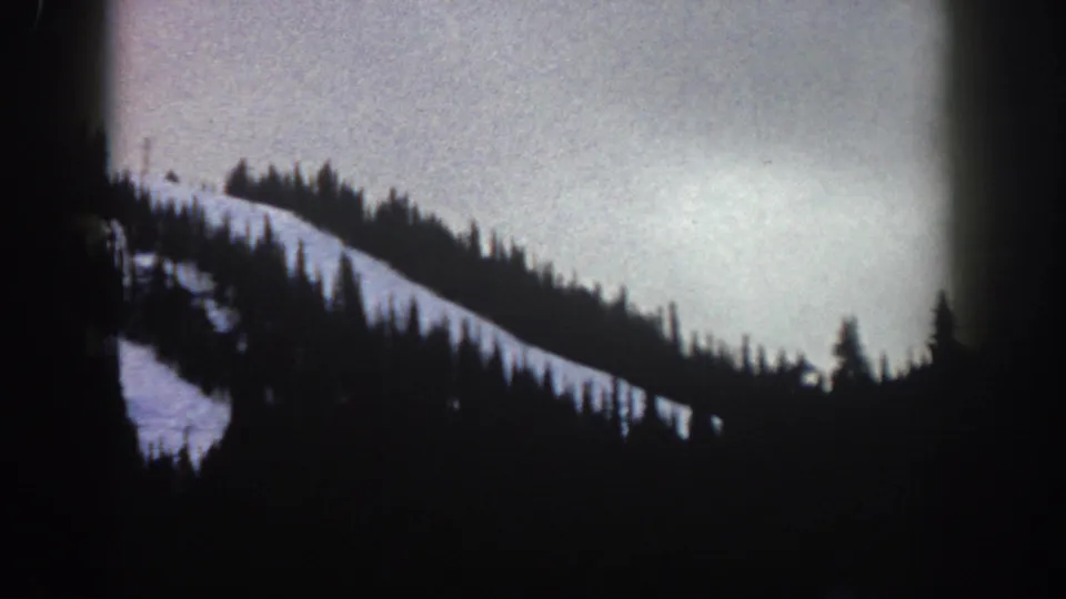 Underexposed 8mm frame of a silhouetted evergreen ridge over a snow-covered hillside in the Aspen, Colorado area, circa 1961.