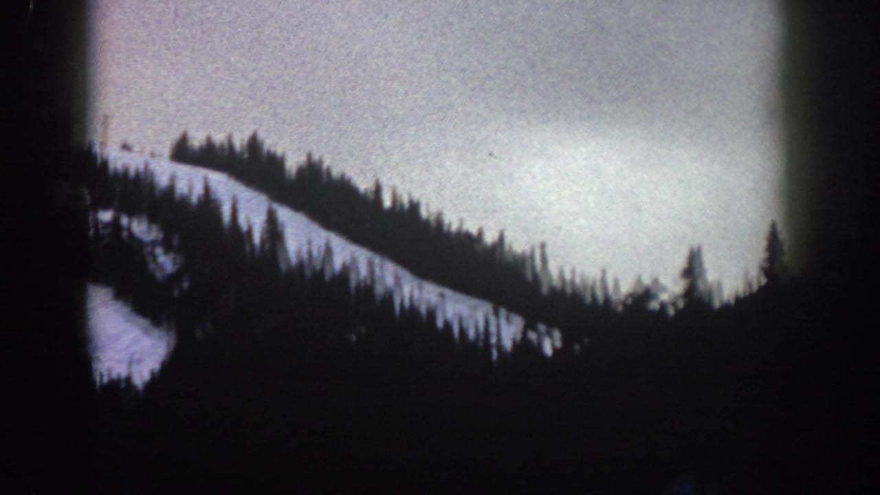 8mm home movie view from a cable car at Aspen, Colorado, circa 1961 — wide snow slope and evergreen treeline under an overcast sky.