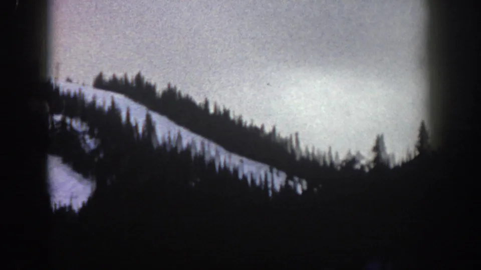 8mm home movie view from a cable car at Aspen, Colorado, circa 1961 — wide snow slope and evergreen treeline under an overcast sky.