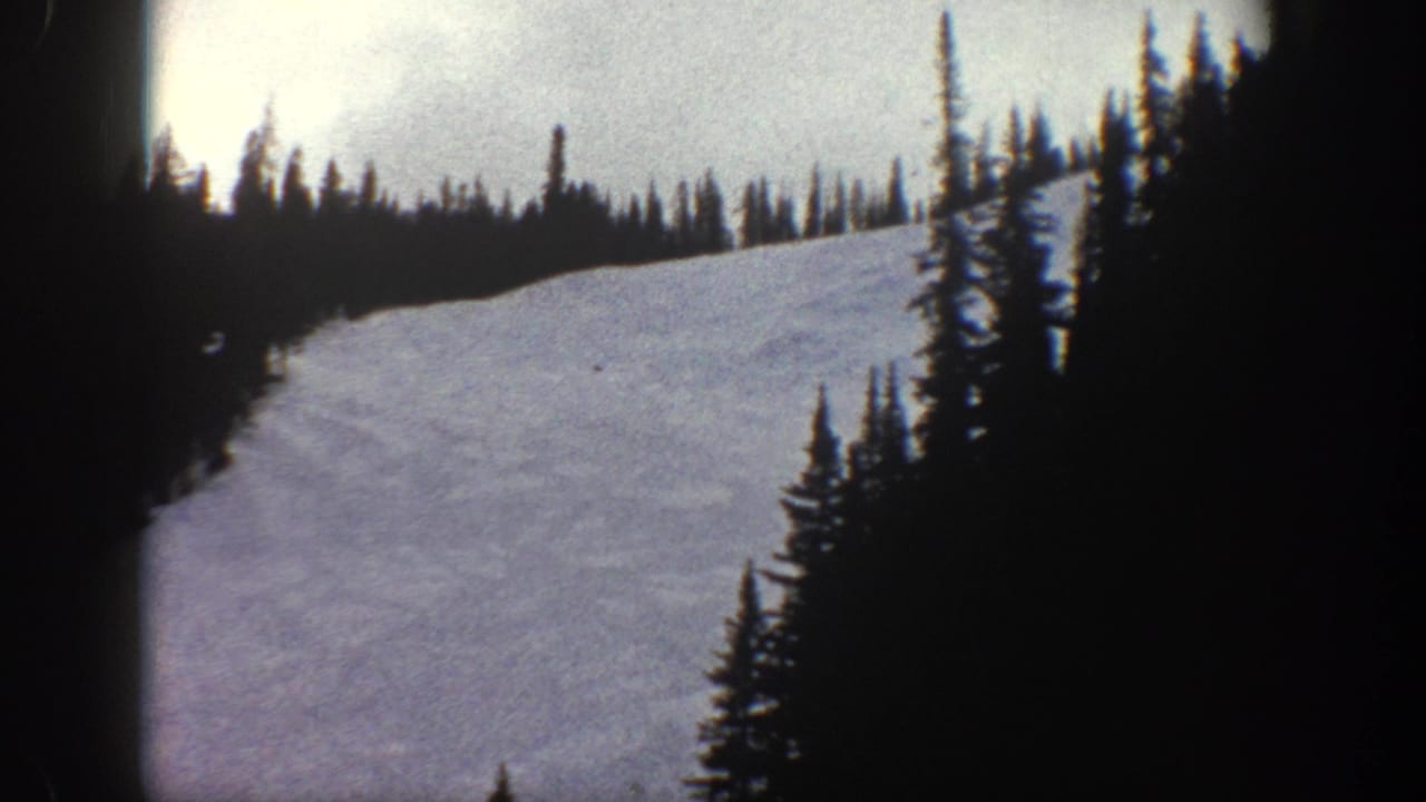 Wide ski run descending between conifer-lined ridges, shot from a moving cable car, with heavy vignetting on frame edges.