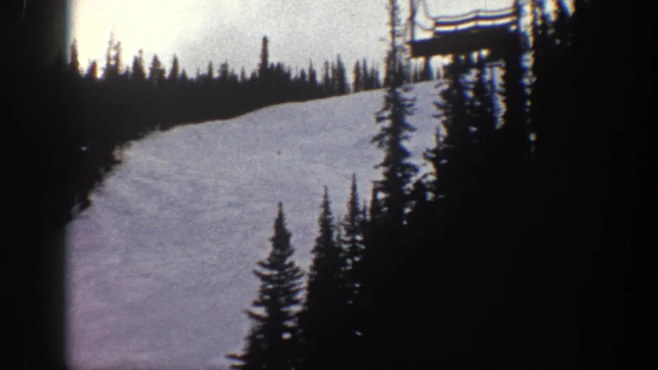 Final 8mm frame from a cable car at Aspen, Colorado, 1961 — ski slope with evergreen trees and a ski lift tower structure entering the upper right of frame.