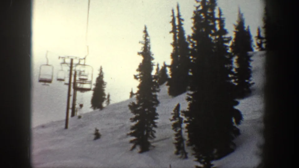 8mm footage of a chairlift chair on cable above a snowy alpine slope with conifers; metadata indicates Aspen, Colorado, circa 1961.