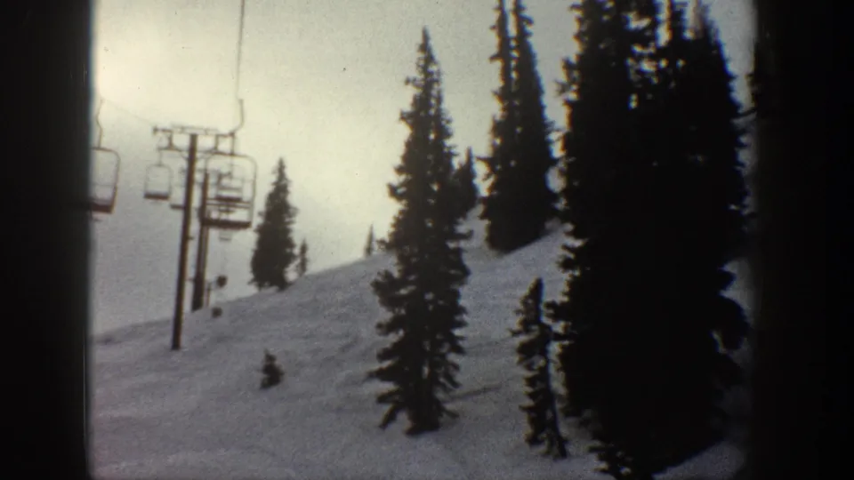 8mm home movie showing multiple chairlift chairs on cables between support poles on a snowy alpine slope, consistent with Aspen Colorado circa 1961.