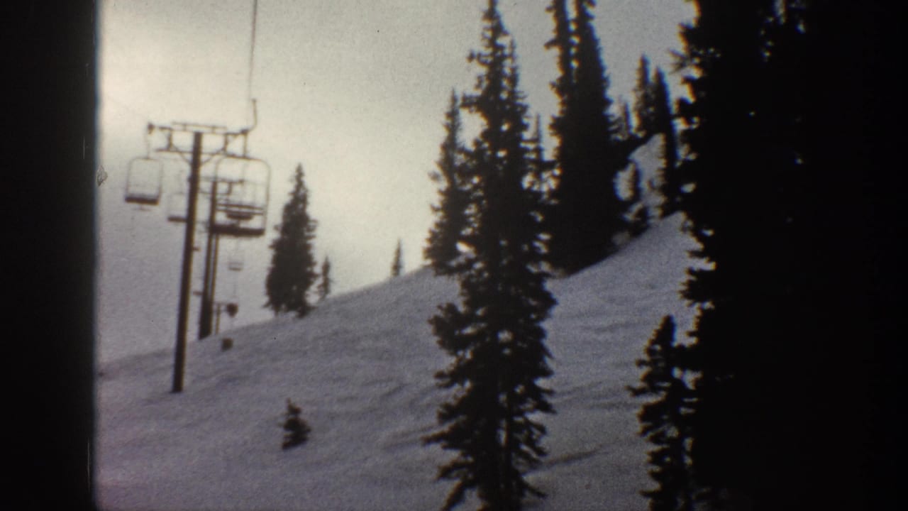Snow-covered ski slope with chairlift cable, hanging chairs, and conifer trees under overcast sky; 8mm film.