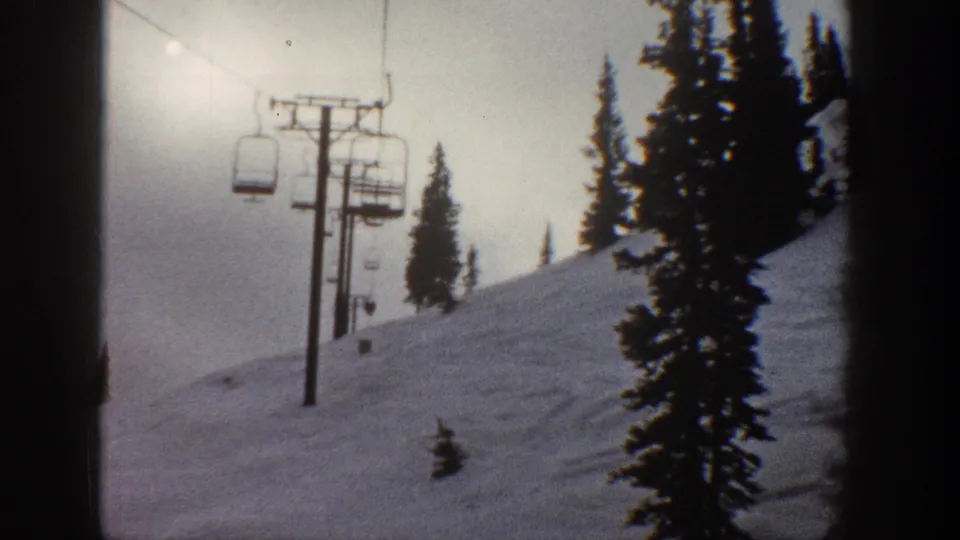 8mm film frame circa 1961 showing two chairlift chairs and a support pole on a snowy ski slope with a sun orb upper right, possibly Aspen, Colorado.