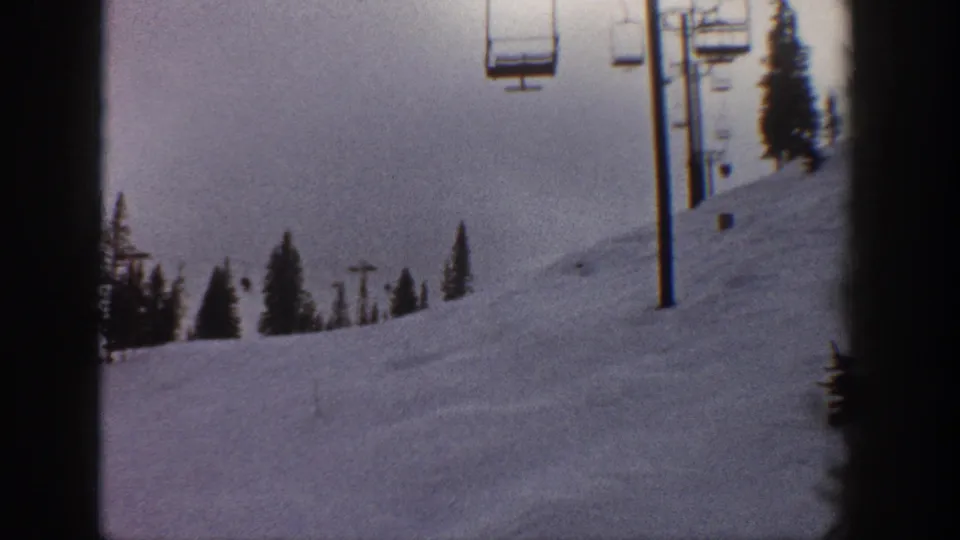 8mm film frame circa 1961 showing a chairlift line with multiple chairs receding across a snowy slope; pinkish sky from age-shifted film stock, possibly Aspen, Colorado.