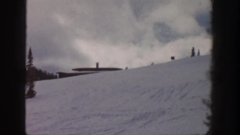8mm frame of a snow slope, possibly Aspen, Colorado, 1961; small unresolved shapes near a low station building suggest possible figures among lift infrastructure.