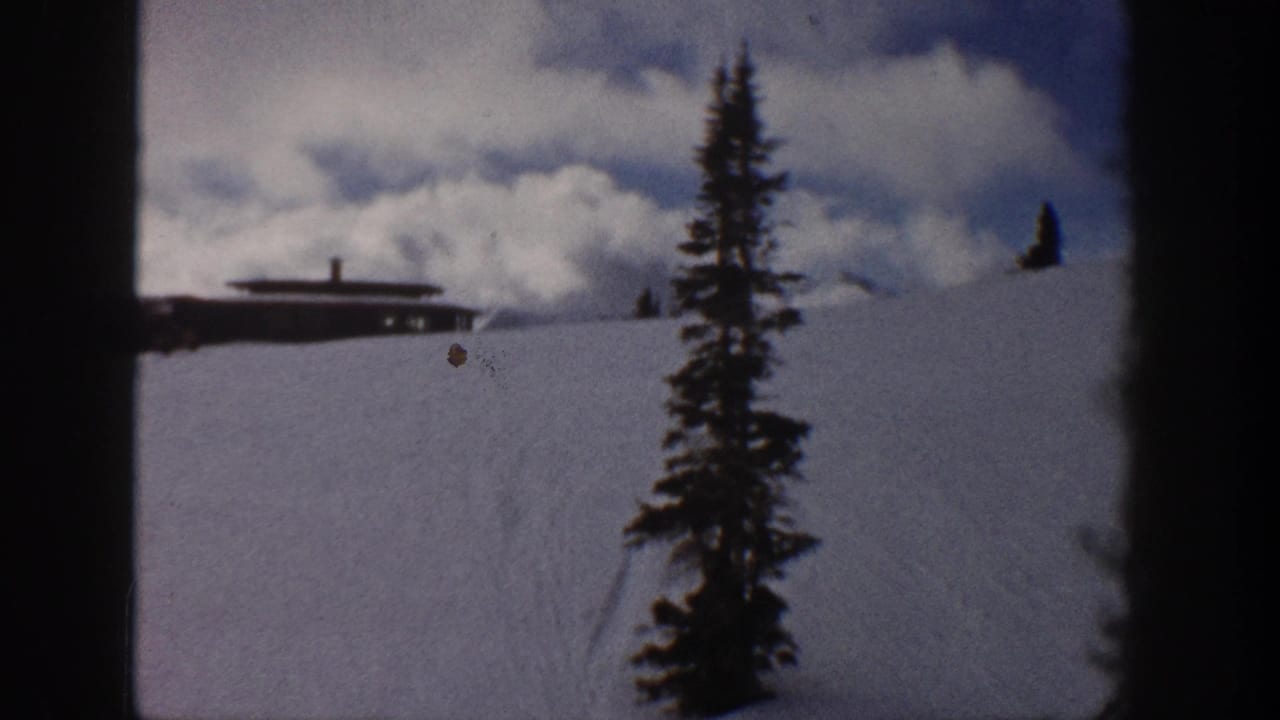 8mm home-movie frame from Aspen, Colorado, circa 1961 — evergreen tree in foreground, flat-roofed cabin on snowy slope, dramatic cumulus clouds above.