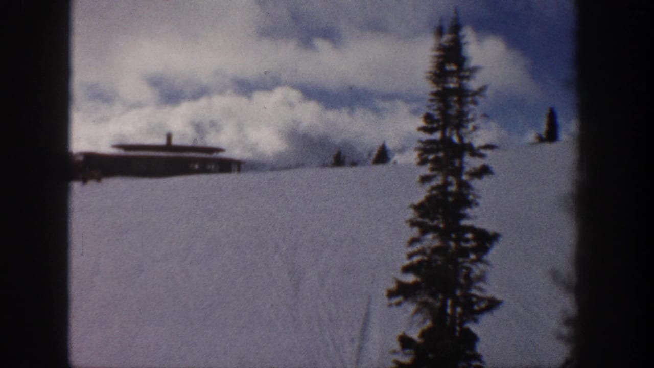 8mm pan frame from Aspen, Colorado, 1961 — cabin on snowy slope, evergreen tree moving right as camera pans, dramatic cloud formation above.