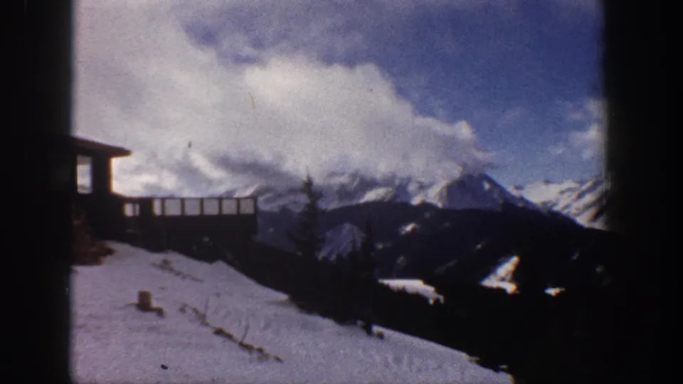 8mm home movie pan showing snow-capped peaks, billowing clouds, and a wooden deck railing at upper left; attributed to Aspen, Colorado, 1961.