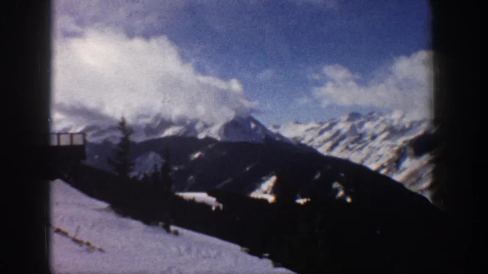 8mm home movie closing frame of a snow-capped mountain ridge with sparse dark trees and faint railing remnant at lower left; attributed to Aspen, Colorado, 1961.