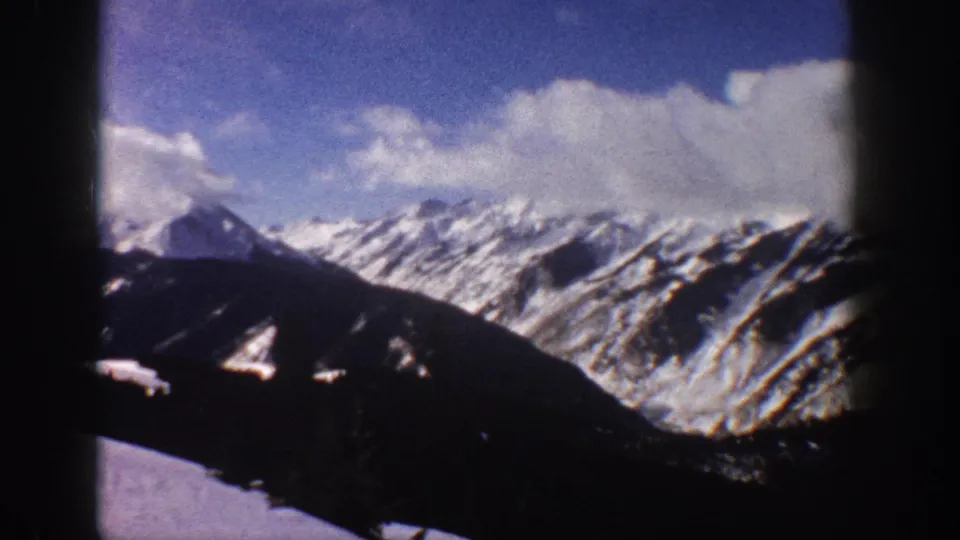 Wider pan of snow-laden Rocky Mountain slopes near Aspen, Colorado, circa 1961, on 8mm home movie film, revealing valley terrain and possible ski-run clearings on the mountain face.