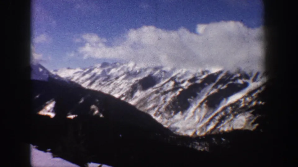Continuing pan of snow-covered Rocky Mountain terrain near Aspen, Colorado, circa 1961, on 8mm home movie film, showing peaks, valley slopes, and possible cleared terrain on the mountain face.